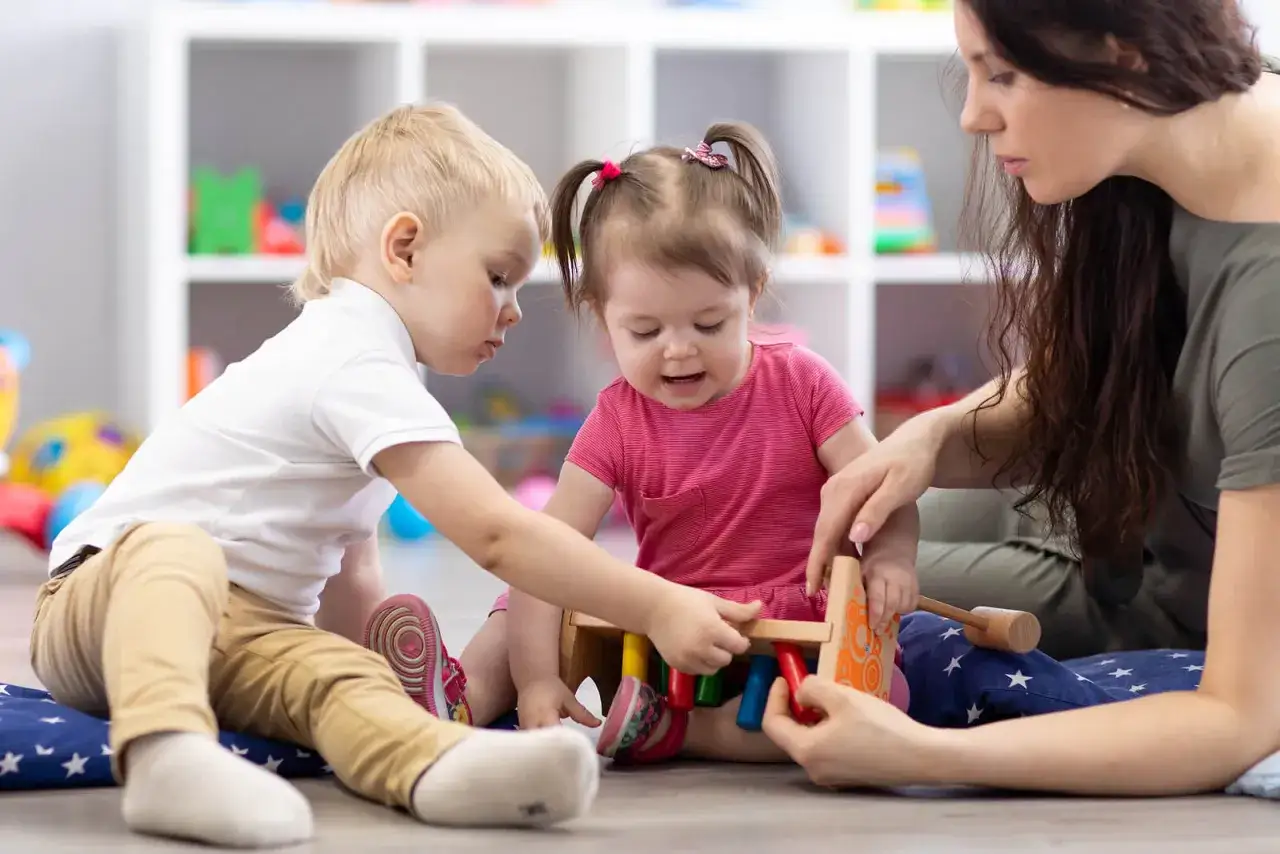Niños y adulto interactúan con un juguete, demostrando el **nivel pragmático del lenguaje** al compartir y cooperar en el juego.