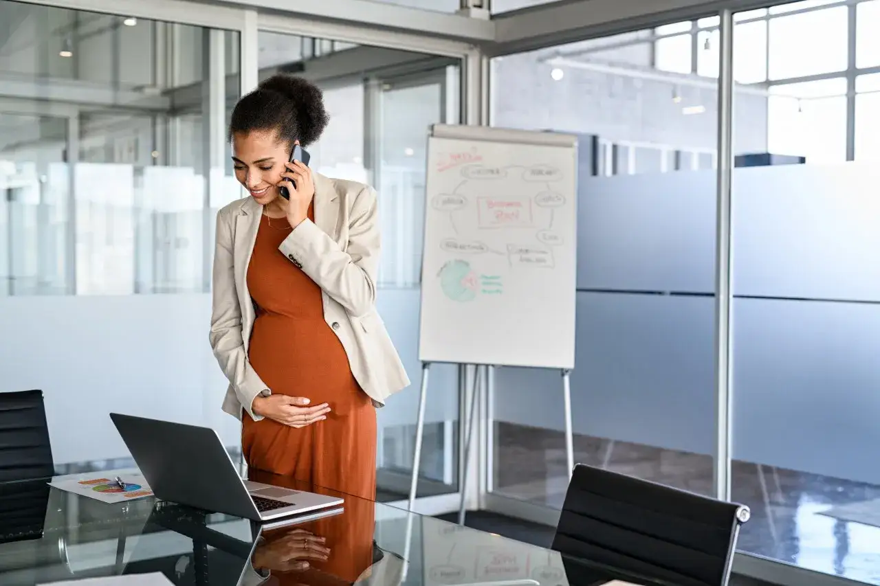 Femme enceinte au téléphone, discutant de la réduction du temps de travail pour la grossesse, devant un tableau blanc.