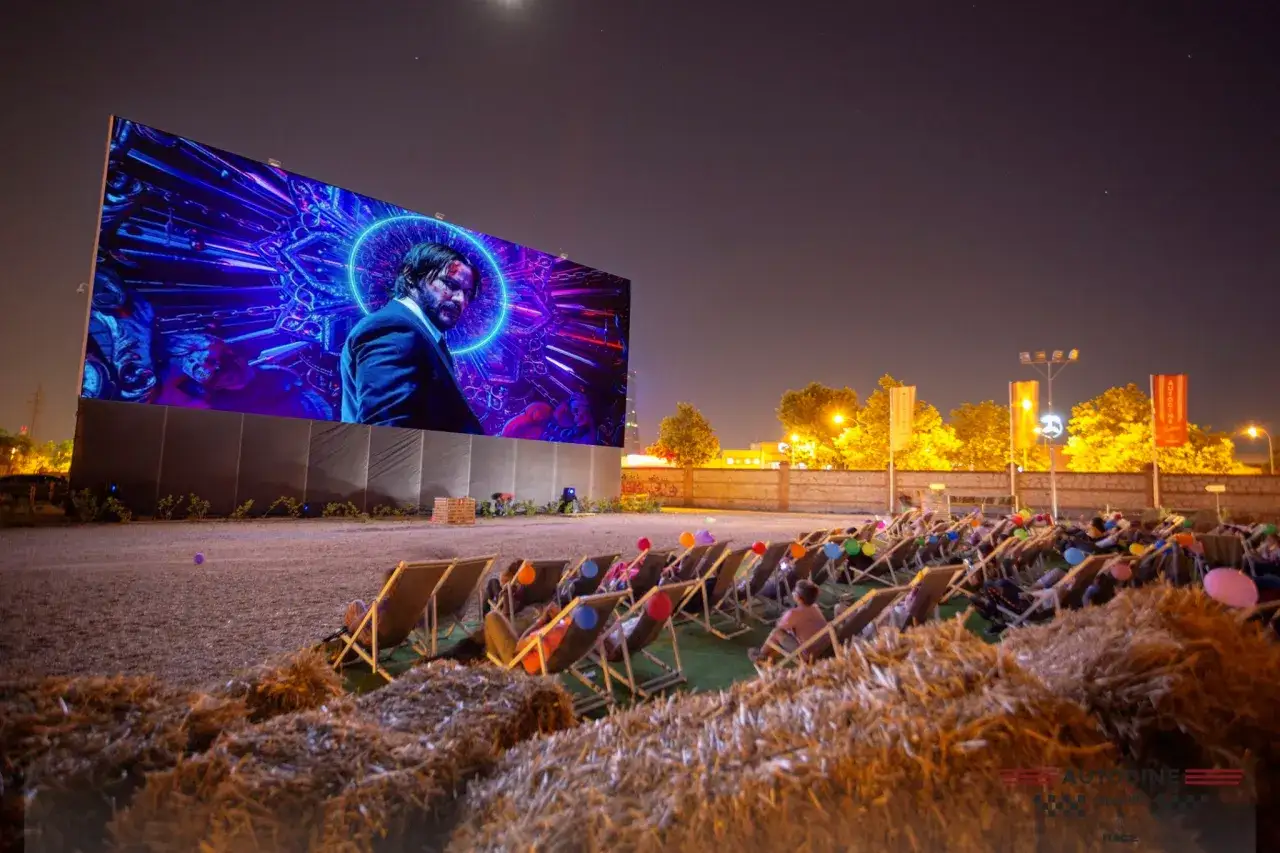 Noche de cine al aire libre en Valencia. Gente relajada en tumbonas viendo una película en pantalla gigante, con globos de colores.