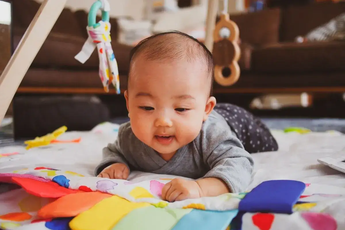 Bambino di 1 mese in posizione prona su un tappetino colorato, esplora i suoi primi giochi. Attività neonato 1 mese.