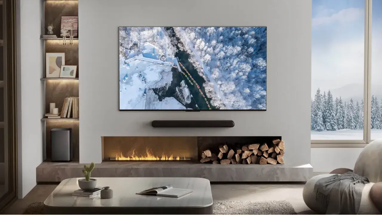 Nowoczesny salon z kominkiem i telewizorem TCL 55C7K, na kt&oacute;rym wyświetlany jest zimowy krajobraz.