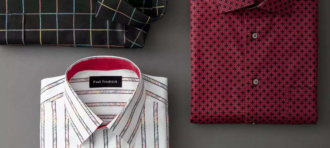 A black plaid shirt with rainbow stitching, a white striped shirt with colorful accents, and a red patterned shirt showcase a variety of dress shirt colors.