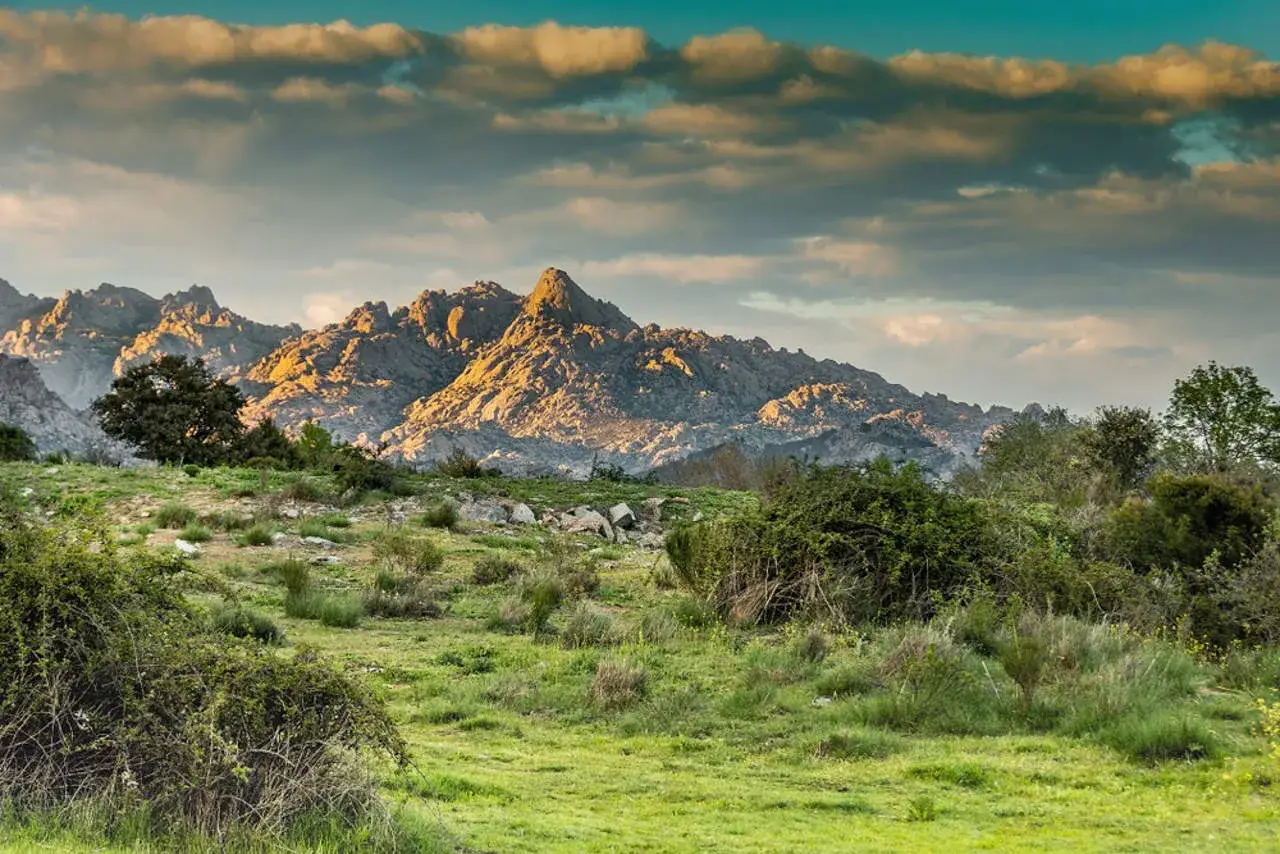 Paisaje montañoso con rocas doradas por el sol, ideal para excursiones cerca de Madrid. Nubes dramáticas en el cielo.