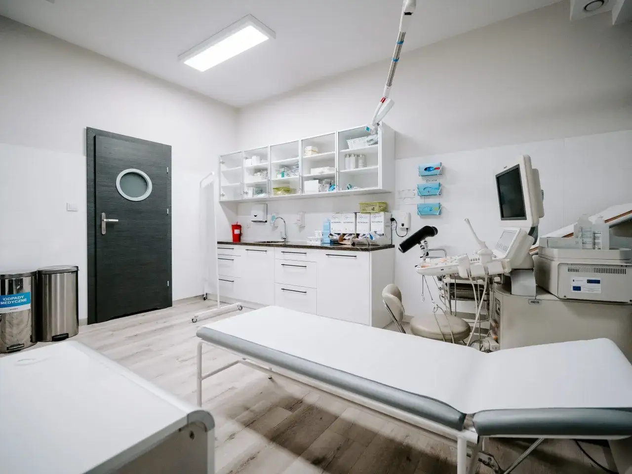 Gabinet dermatologiczny z kozetkami, aparaturą USG i szafkami medycznymi.