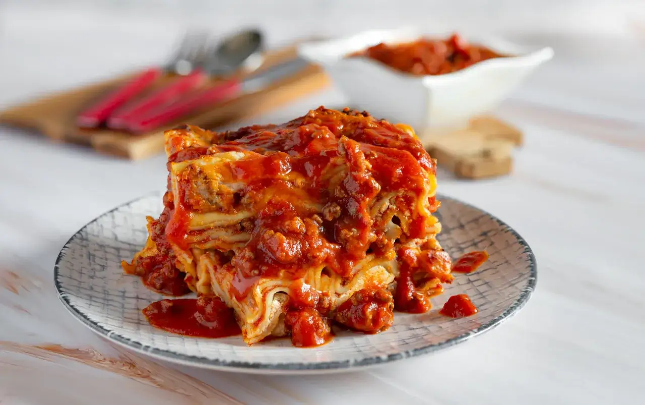 Una fetta di lasagna salentina ricca e succulenta, con strati di pasta, rag&ugrave; e besciamella, servita su un piatto decorato.
