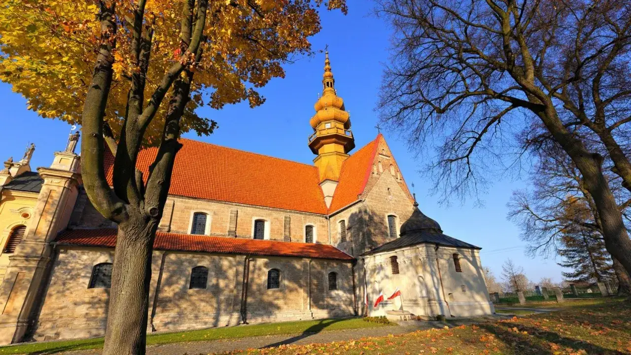 Kamienna świątynia z pomarańczowym dachem i złotą wieżą, otoczona jesiennymi drzewami. To kości&oacute;ł św. Zbigniewa.