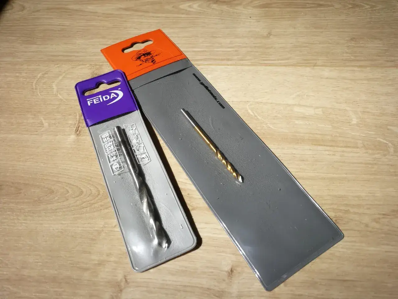 Zwei Metallbohrer, einer in violetter, der andere in orangefarbener Verpackung, bereit zum Plexiglas bohren.