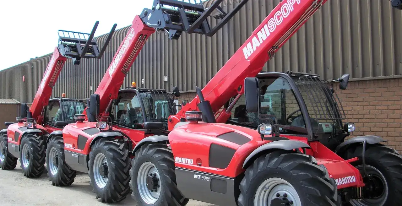 Rzędy czerwonych ładowarek teleskopowych Manitou, gotowych do pracy. Posiadanie uprawnień na manitou to klucz do efektywnego transportu materiałów.