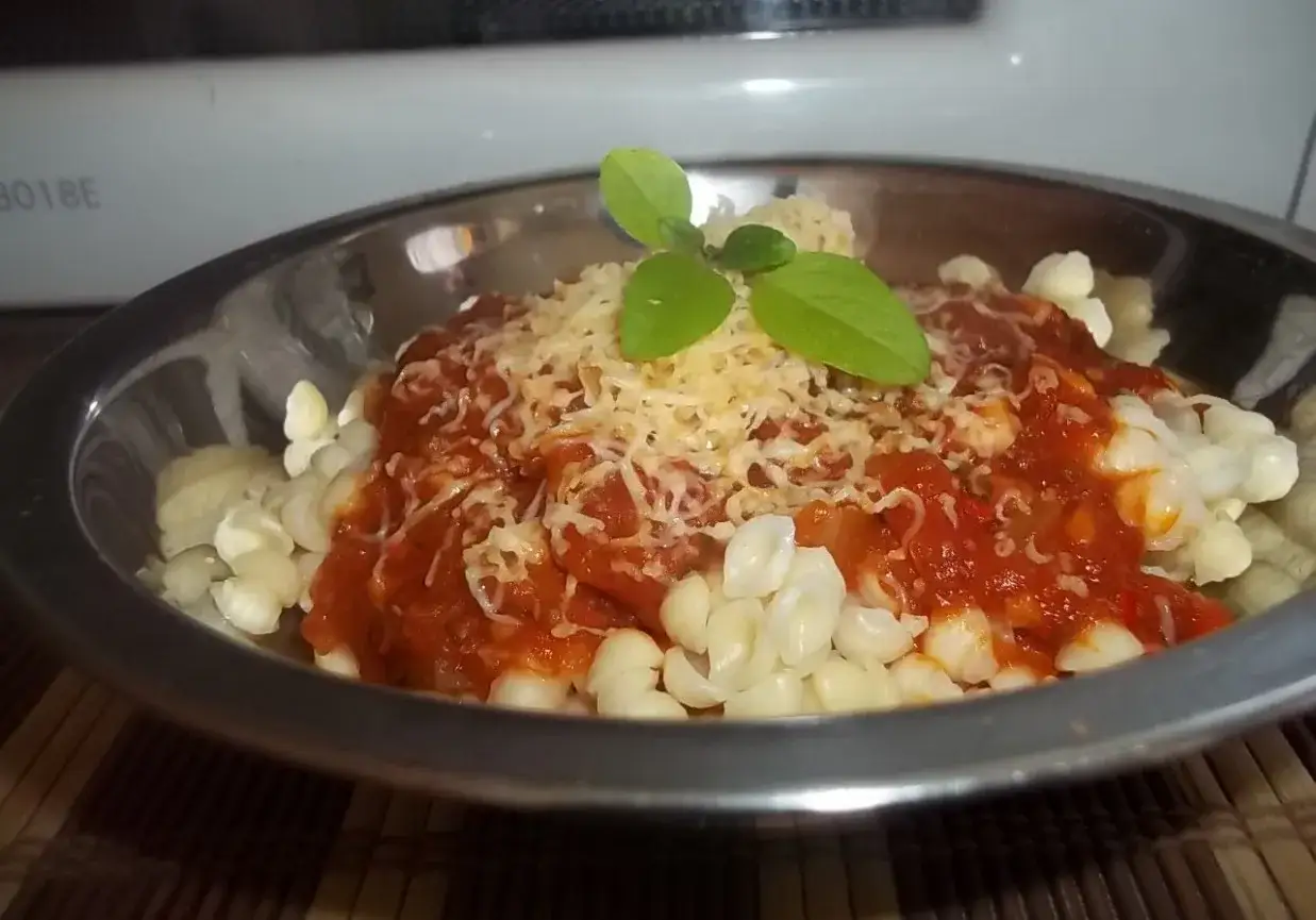 Pyszny makaron z sosem do spaghetti, posypany startym parmezanem i udekorowany listkami bazylii.