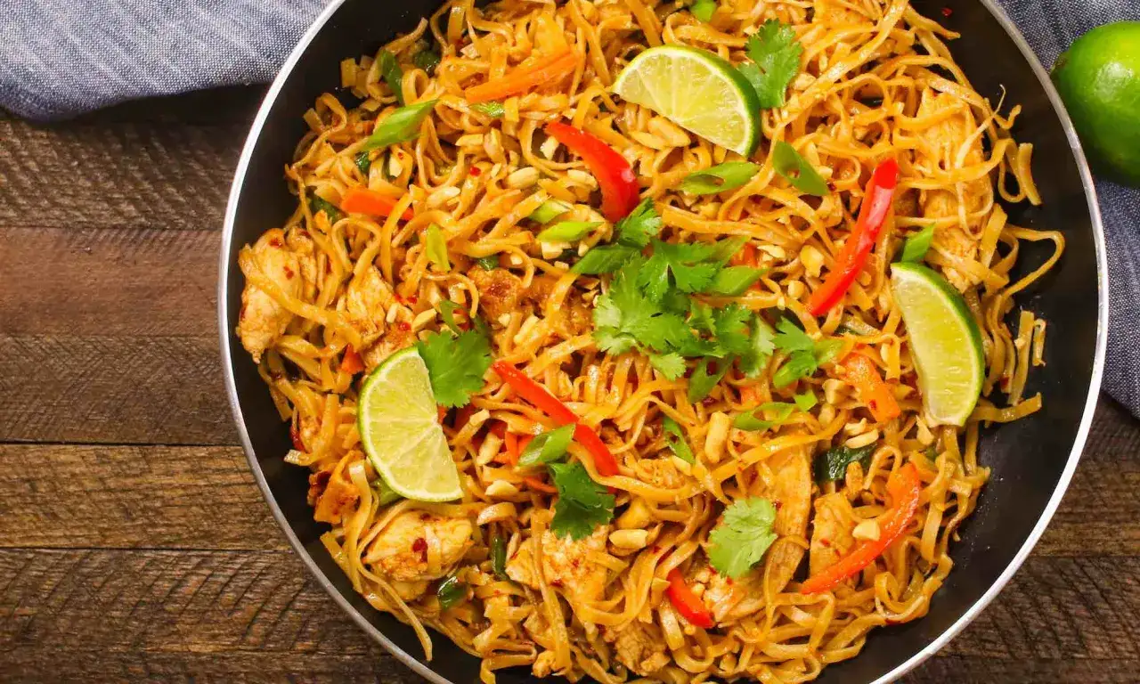 En l&auml;cker kyckling pad thai i en stekpanna, toppad med limeklyftor, koriander och jordn&ouml;tter. En perfekt m&aring;ltid!