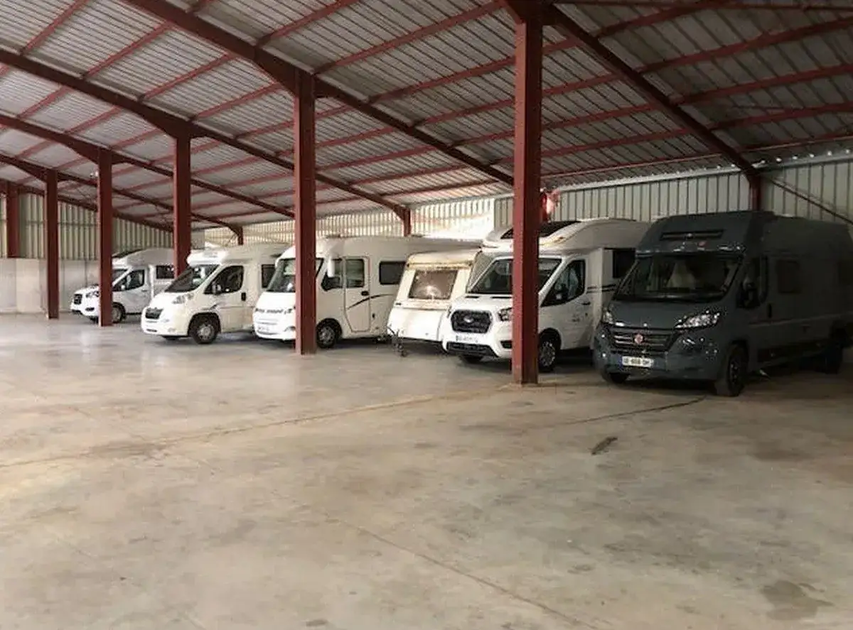 Plusieurs camping-cars et une caravane sont garés dans un entrepôt, prêts pour leur hivernage.