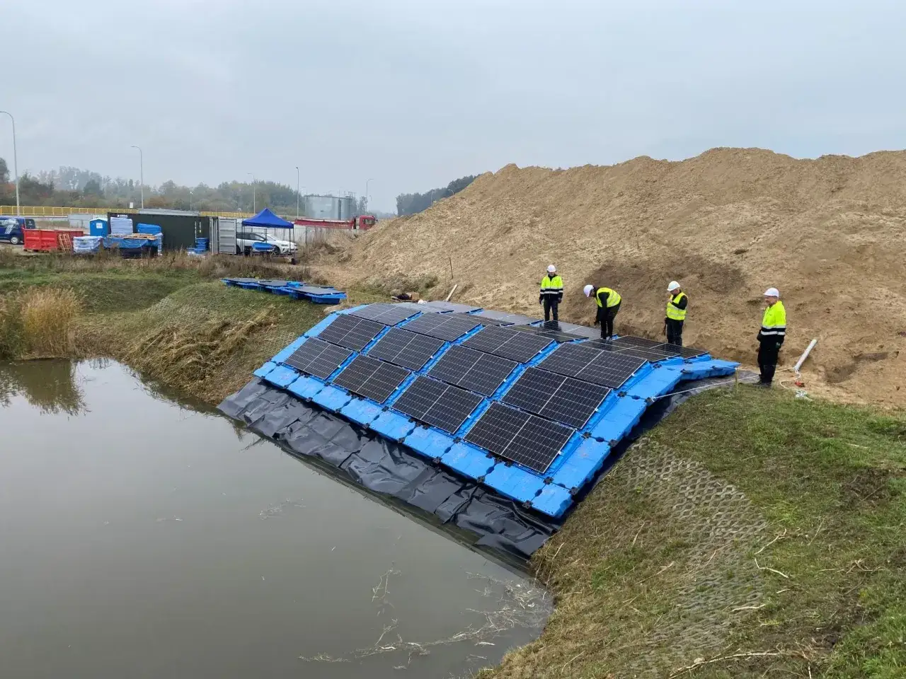 Instalacja fotowoltaiki na wodzie. Pracownicy w kamizelkach montują panele słoneczne na pływających platformach.