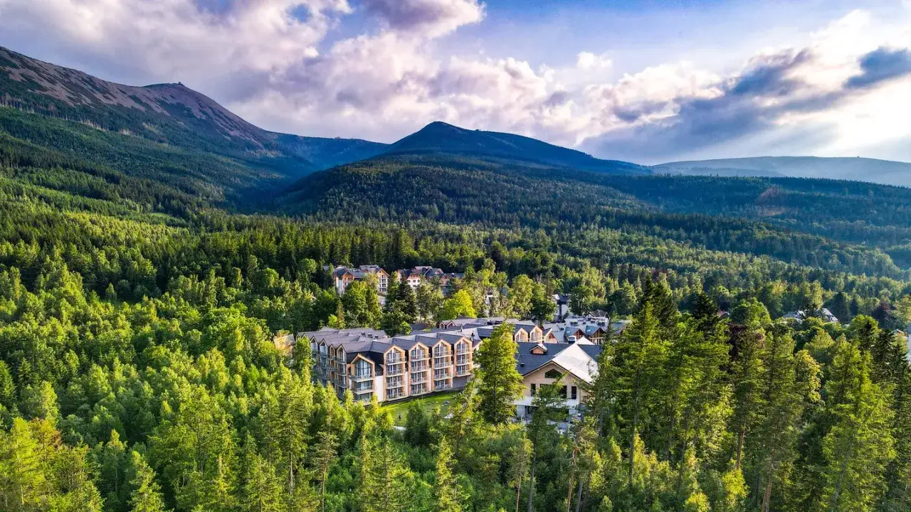 Nowoczesny hotel Karpacz w Karpaczu otoczony zielonym lasem, z górami w tle.