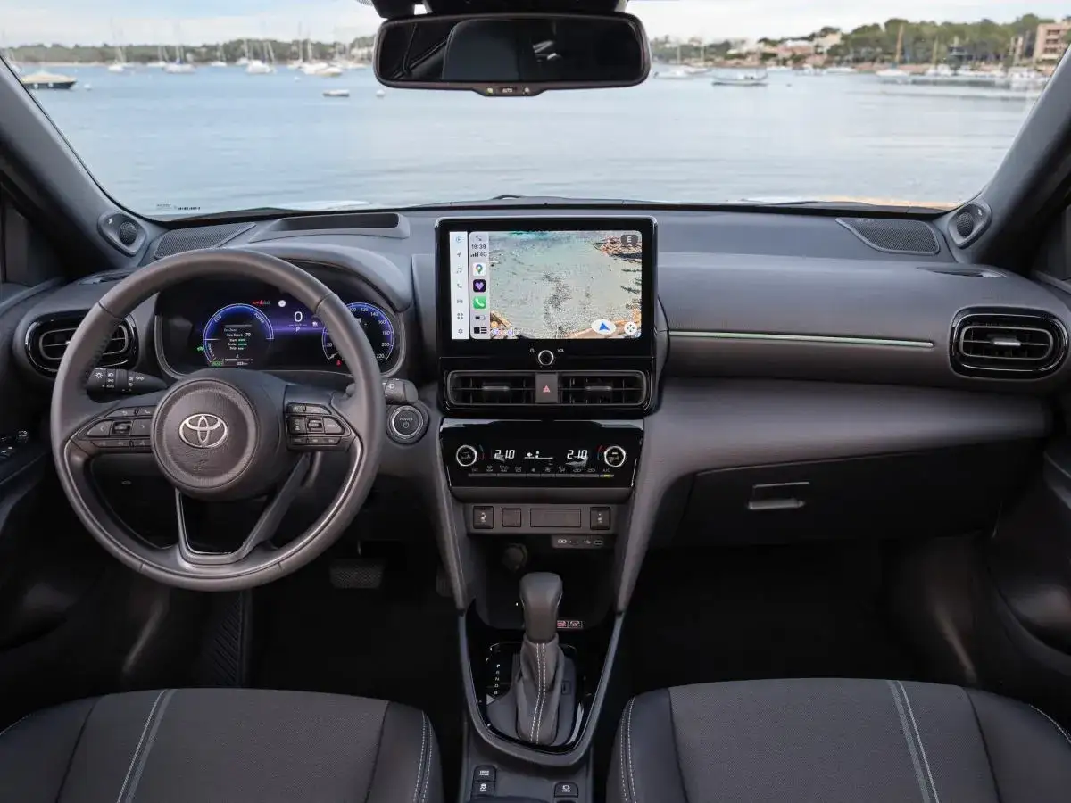 Wnętrze Toyoty Yaris Cross 2024 z ekranem nawigacji pokazującym mapę i widokiem na morze z łodziami.