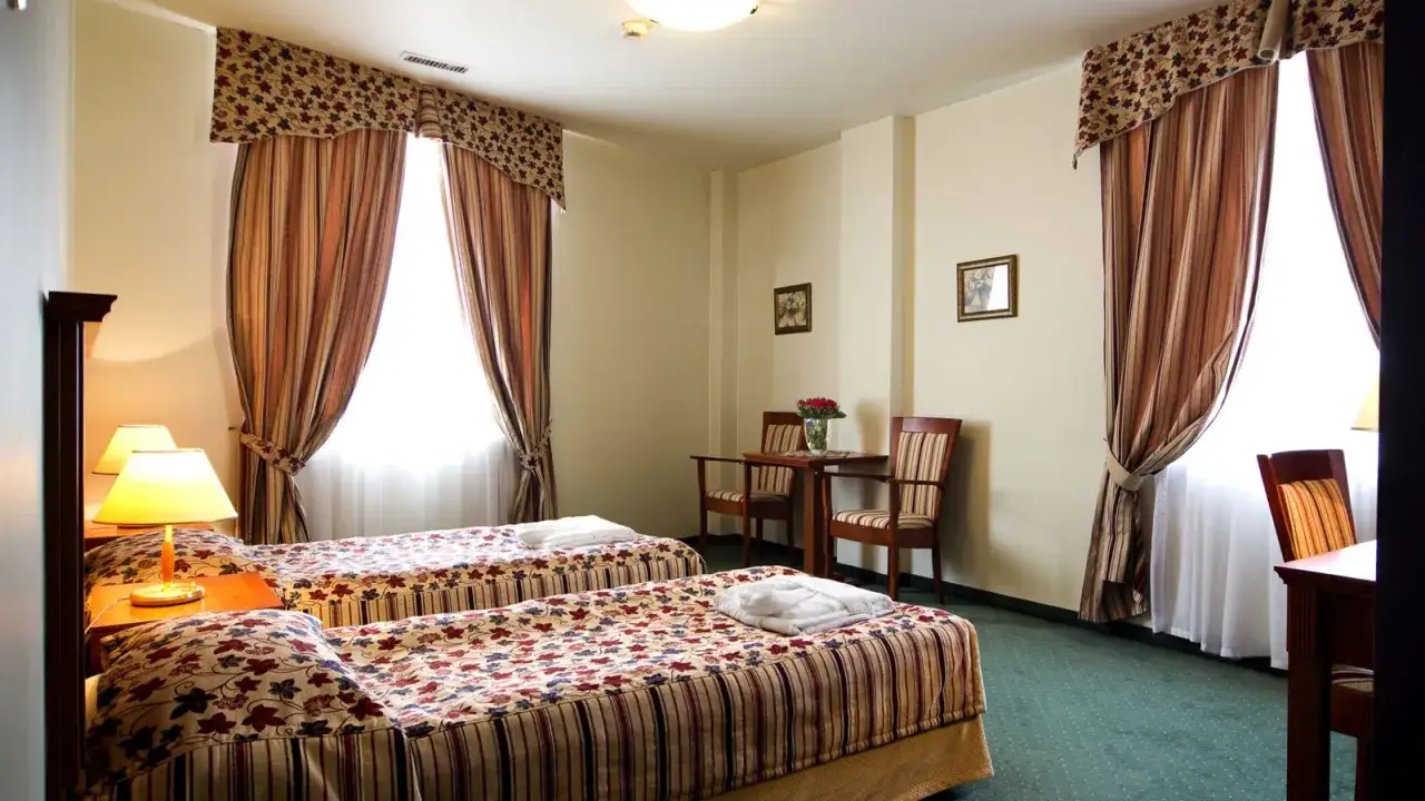 Przytulny pokój hotelowy z dwoma łóżkami, stolikiem i krzesłami. Idealne miejsce na nocleg w hotelu Młyn Włocławek.