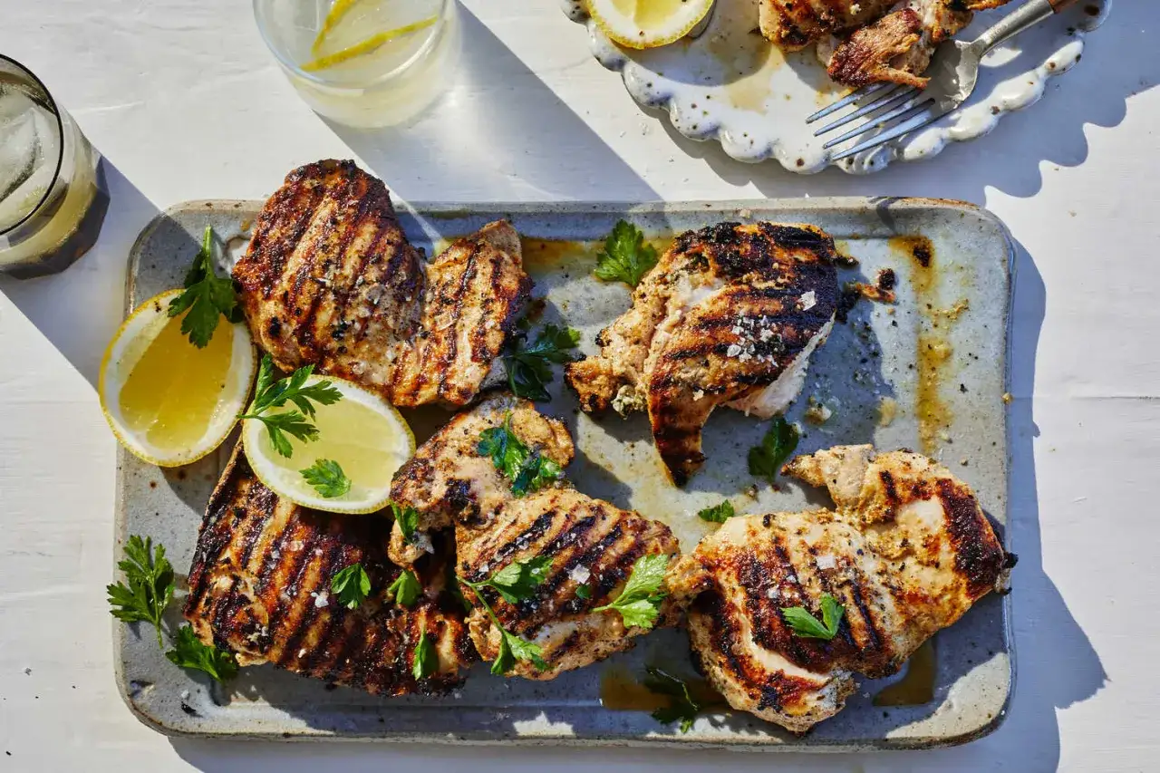 Grillad yoghurtmarinerad kyckling med citronklyftor och persilja p&aring; ett fat. Perfekt f&ouml;r en somrig m&aring;ltid.