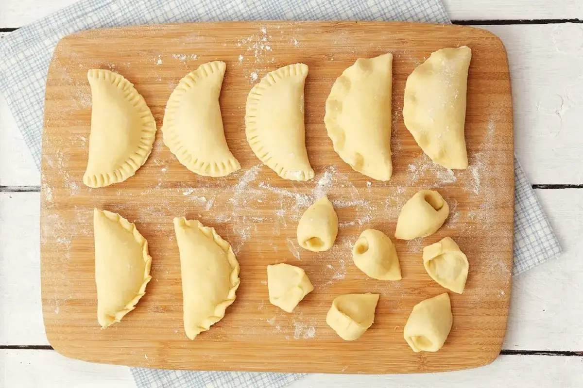 Surowe pierogi i uszka na desce. Zastanawiasz się, czy rozmrażać pierogi przed gotowaniem? Te wyglądają na świeże, gotowe do lepienia.