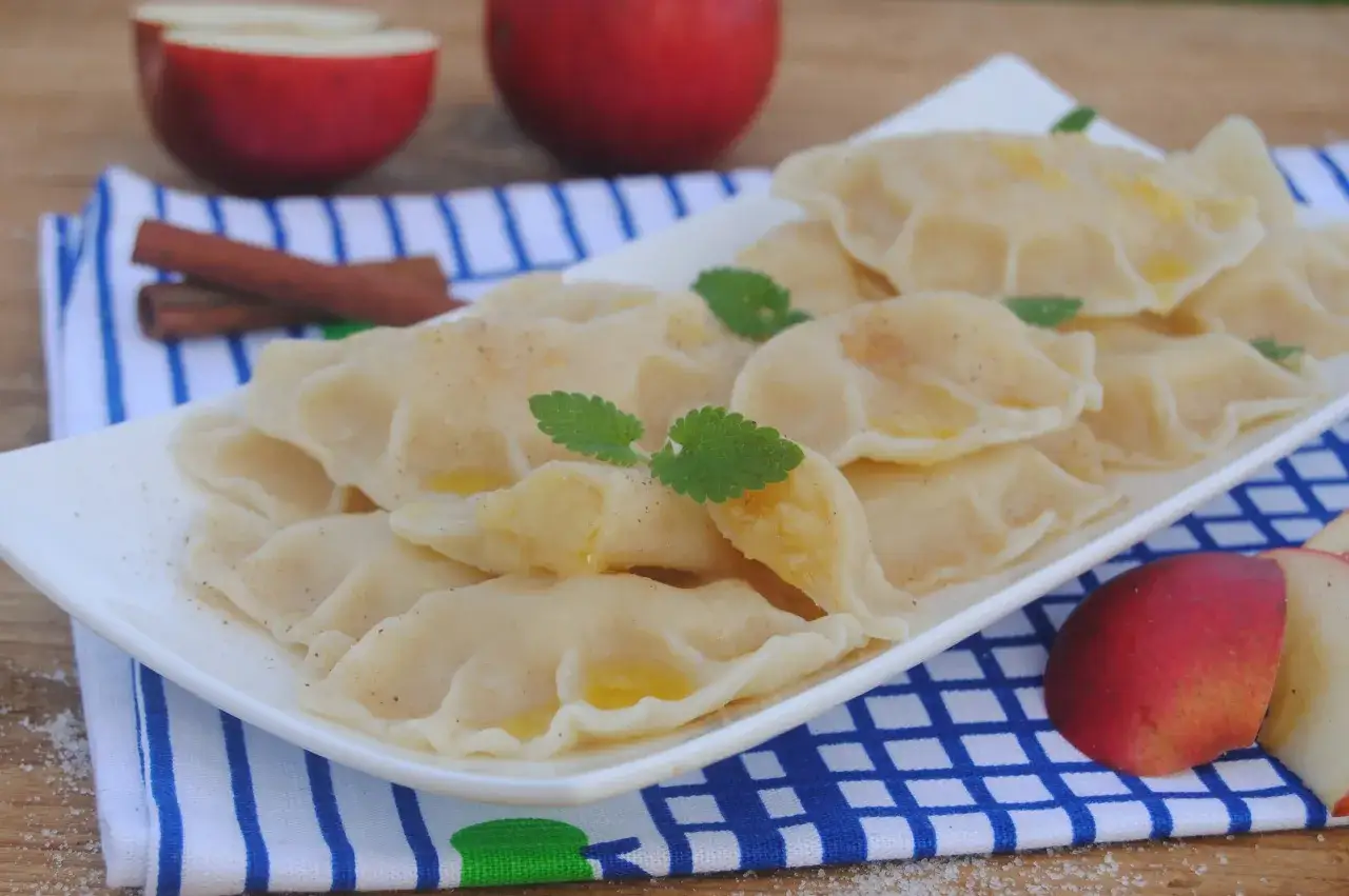 Pyszne pierogi z jabłkami, posypane cynamonem, z jabłkami i laskami cynamonu w tle.