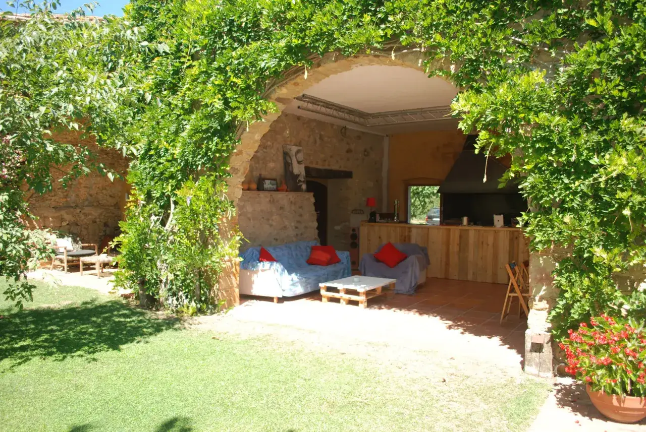 Un patio acogedor con sof&aacute;s y una barra de madera, cubierto por una exuberante madreselva planta.