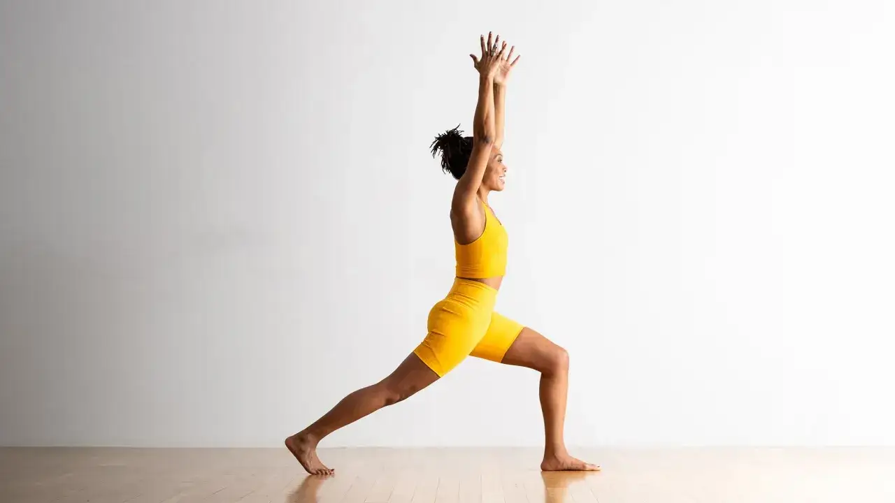 Donna in posa yoga, braccia alzate, gambe divaricate. Lo yoga scolpisce il fisico, tonificando ogni muscolo.