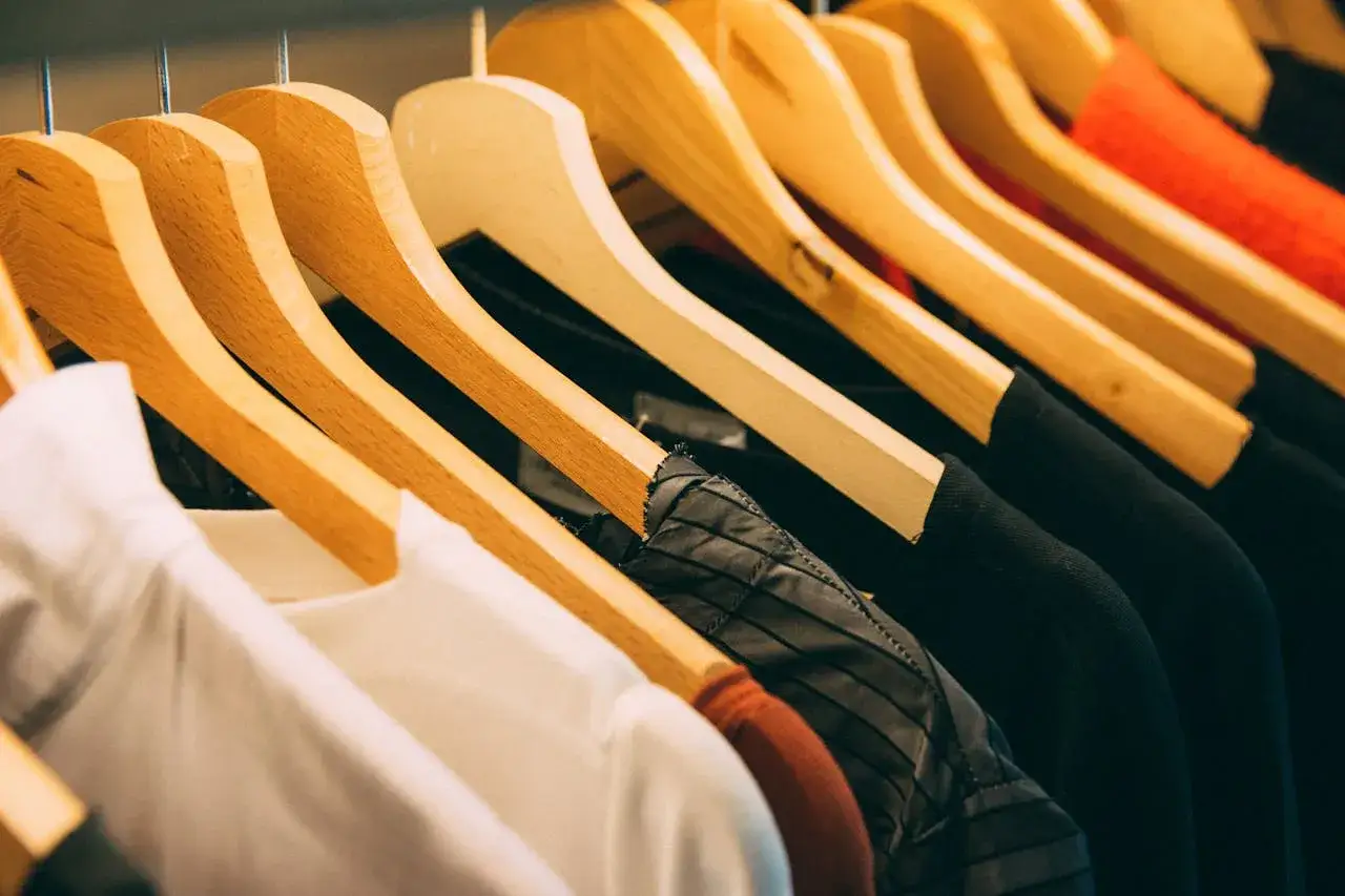 Rzędy ubrań na drewnianych wieszakach, gotowe do sprzedaży w branży retail. Białe, czarne i czerwone tkaniny tworzą estetyczny widok.