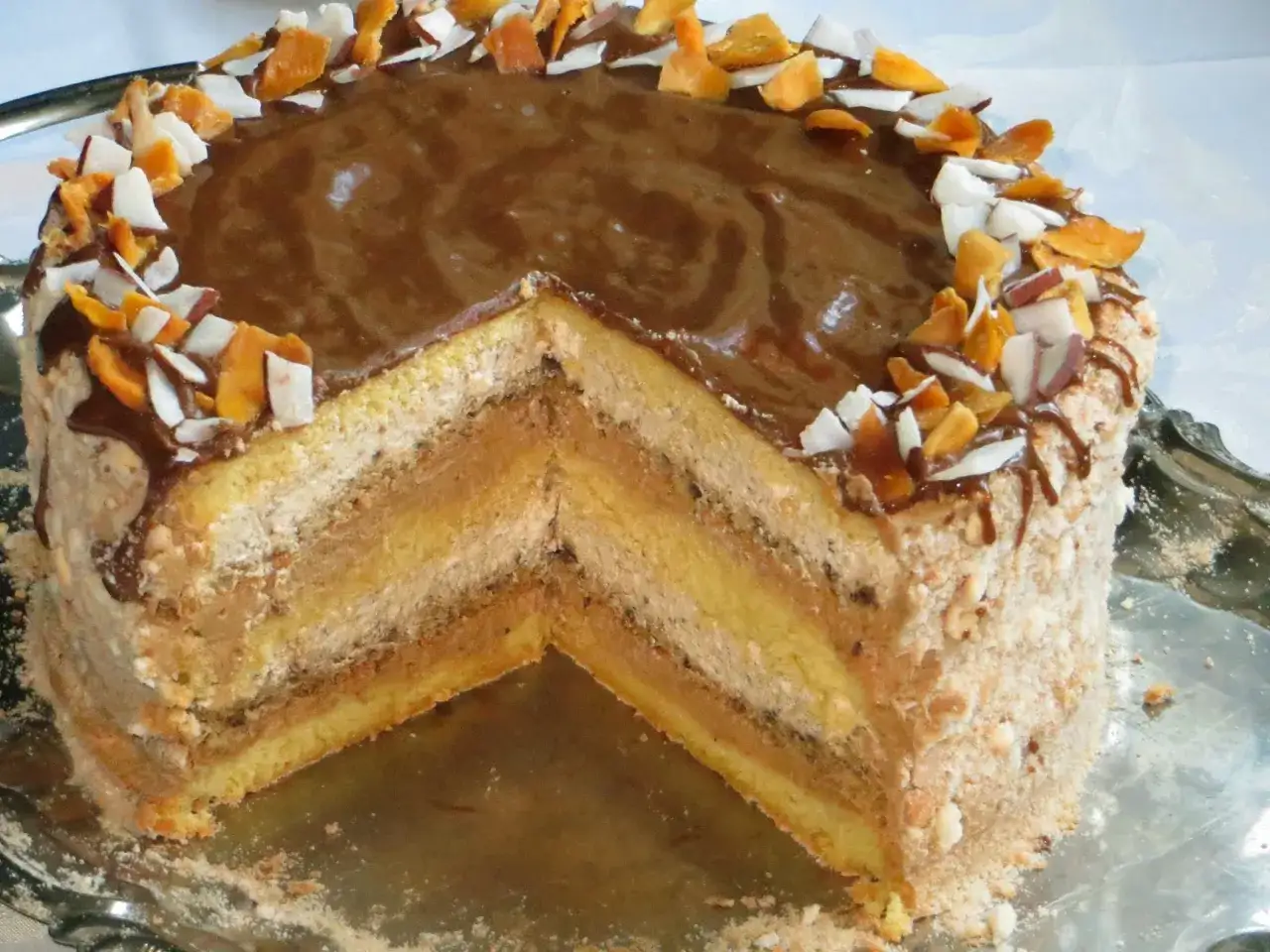 Pyszny tort toffifee z czekoladową polewą, orzechową posypką i wiórkami kokosowymi. Widoczny przekrój ujawnia wiele warstw kremu i biszkoptu.