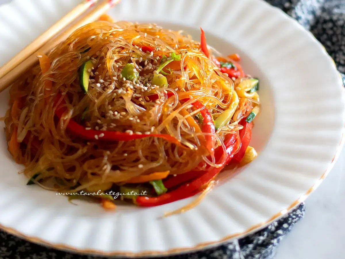 Delicati spaghetti di riso con verdure colorate, peperoni rossi, zucchine e carote, guarniti con semi di sesamo.