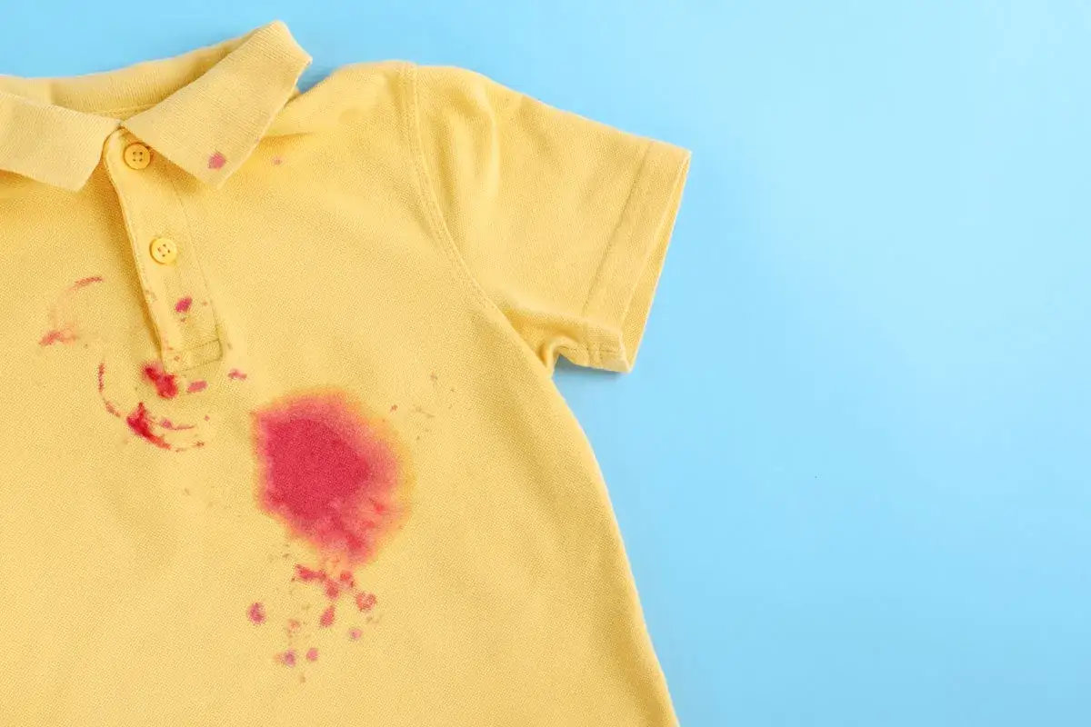 Gelbes Poloshirt mit roten Flecken, die auf eine Herausforderung beim Flecken entfernen hinweisen.
