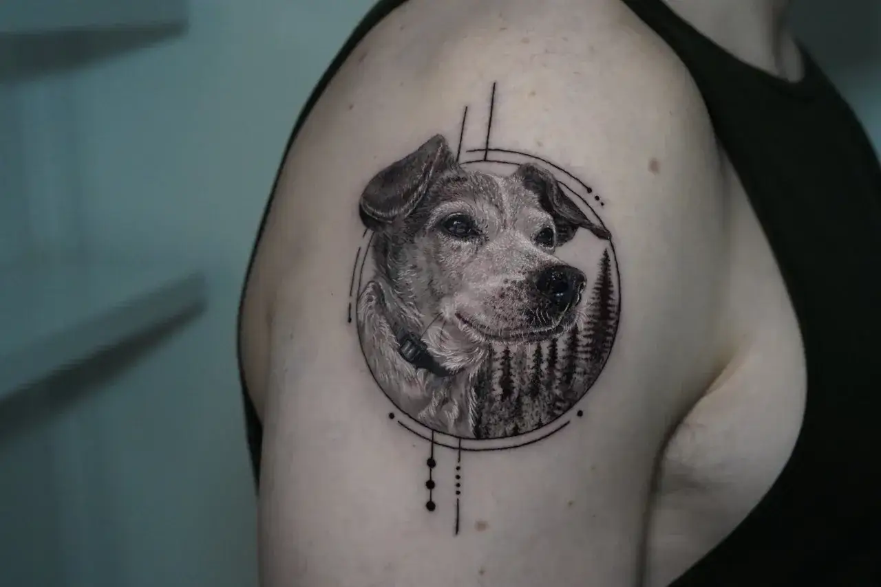 Tatuajes de perros realistas en un hombro, con un diseño circular que incluye un bosque.