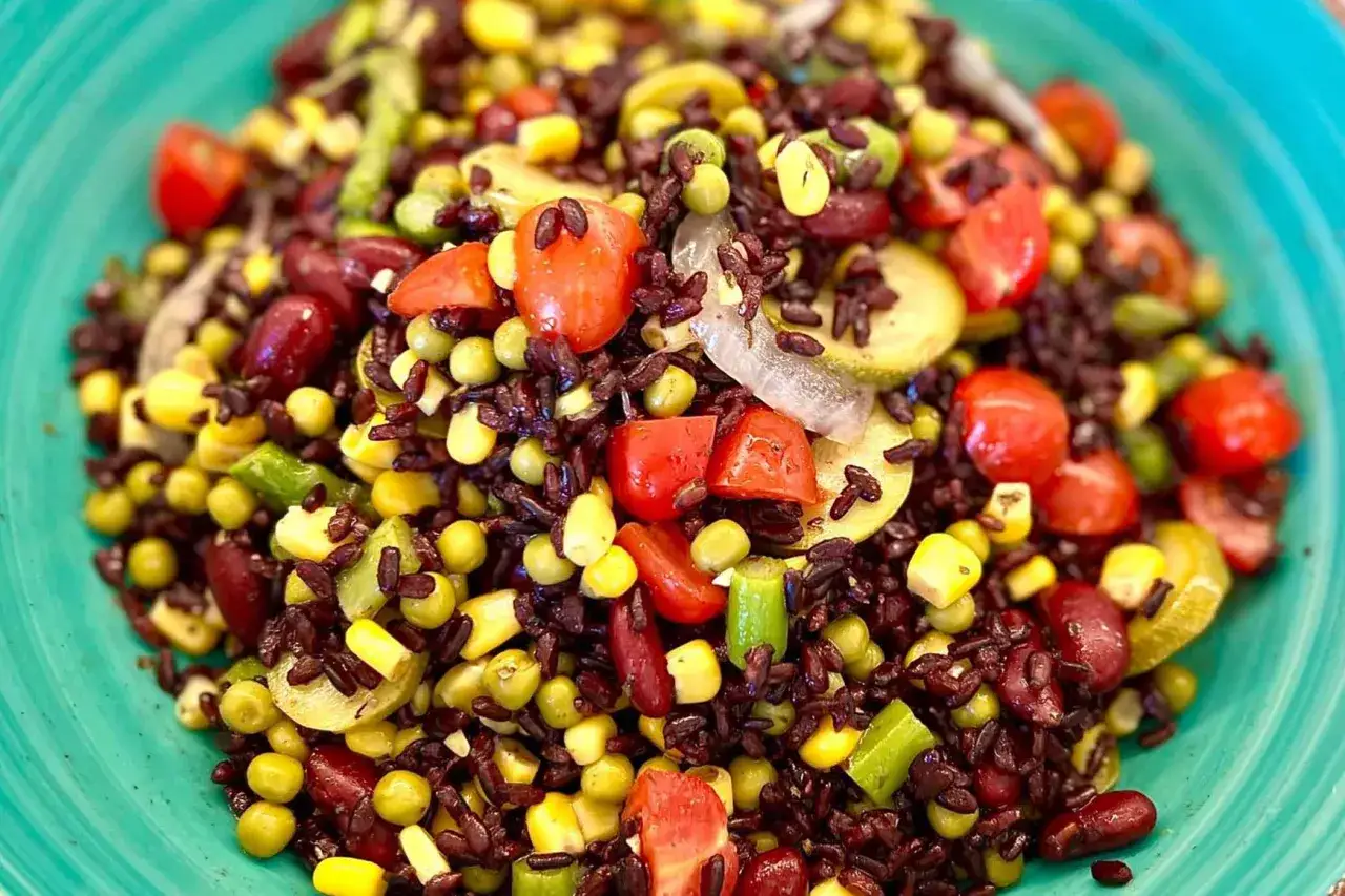 Un'insalata di riso vegetariana colorata con riso nero, pomodorini, mais, piselli e fagioli rossi, servita in un piatto turchese.