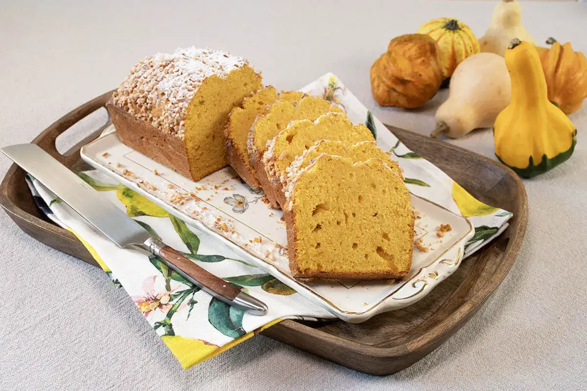 Un delicioso bizcocho de calabaza, cubierto con az&uacute;car glas y trocitos de nuez, servido en una bandeja con calabazas decorativas.