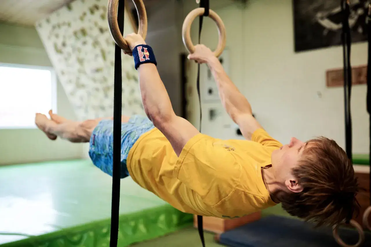 Atleta di calisthenics in posizione di front lever sugli anelli, con polsino Red Bull.