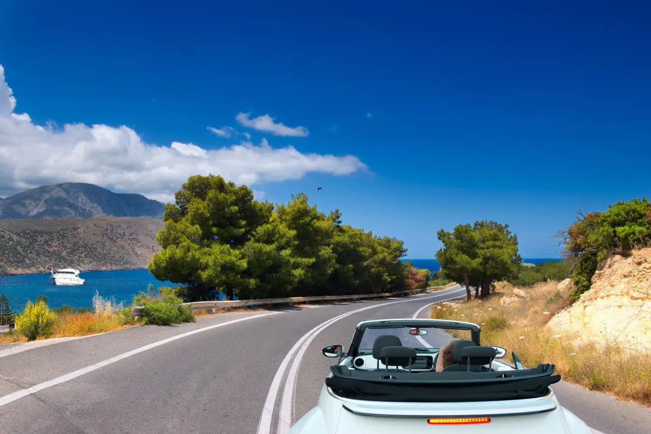 Voiture décapotable sur une route côtière en Grèce, avec la mer bleue et des montagnes en arrière-plan. Le tourisme en Grèce offre des paysages magnifiques.