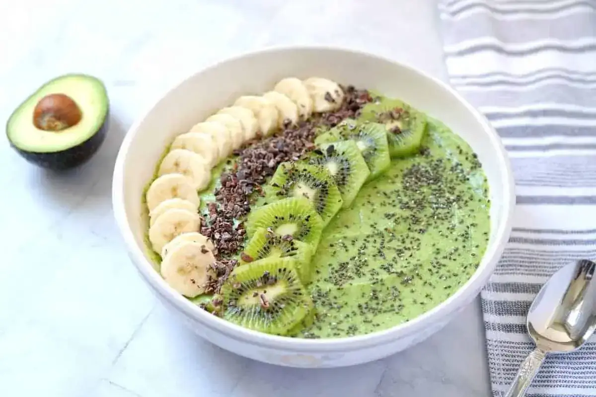 Zielony koktajl z awokado, kiwi i banana, udekorowany plasterkami banana, kiwi, kakao i nasionami chia.