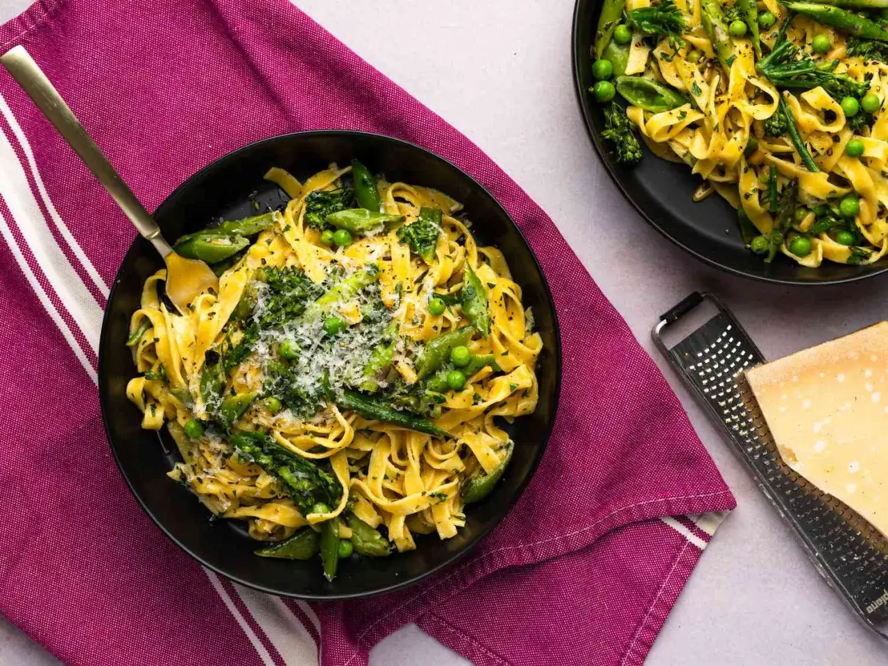 Un plato de pasta primavera con esp&aacute;rragos, guisantes y br&oacute;coli, espolvoreado con queso rallado.