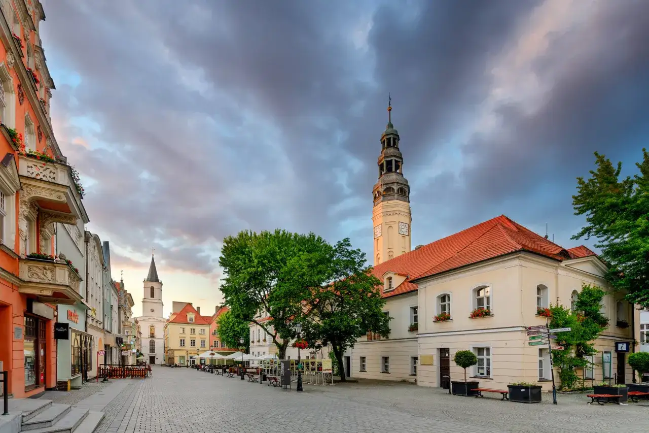 Zielona Góra rynek o wschodzie słońca. Urokliwe kamienice, wieża ratuszowa i kościół tworzą malowniczy widok.