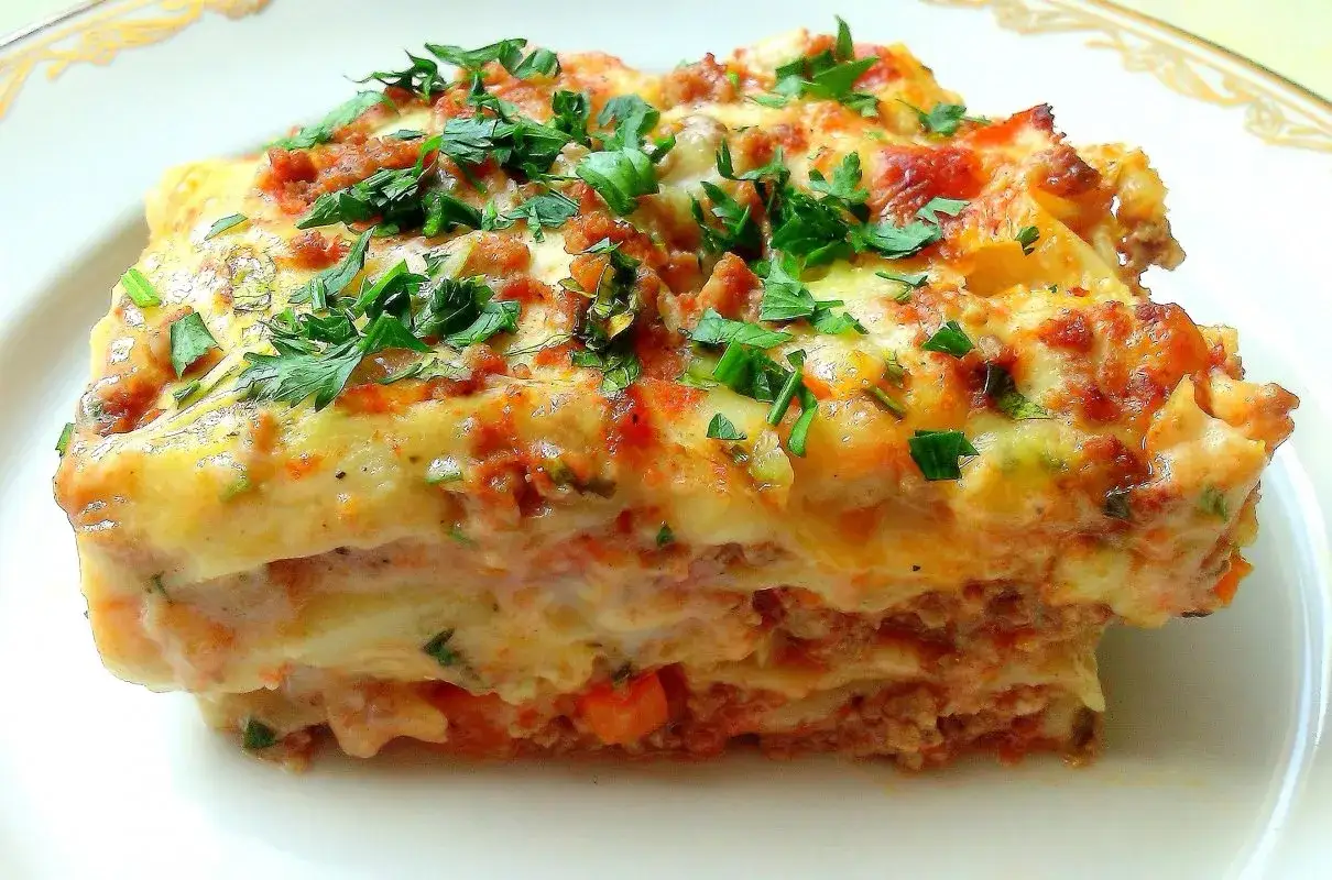 Pyszna lasagne Ani Starmach, z warstwami mięsa, sosu i sera, posypana świeżą natką pietruszki.
