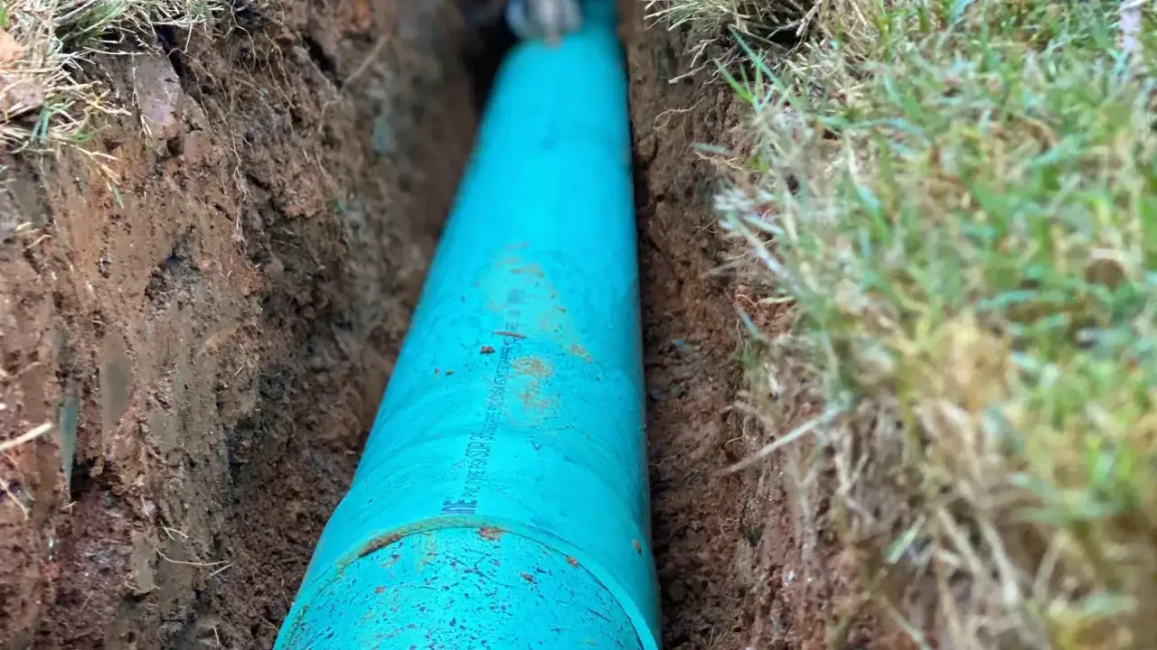 Gros tuyau vert en PVC pour le rejet d'eau, enfoui dans une tranchée de terre avec de l'herbe sur les bords.