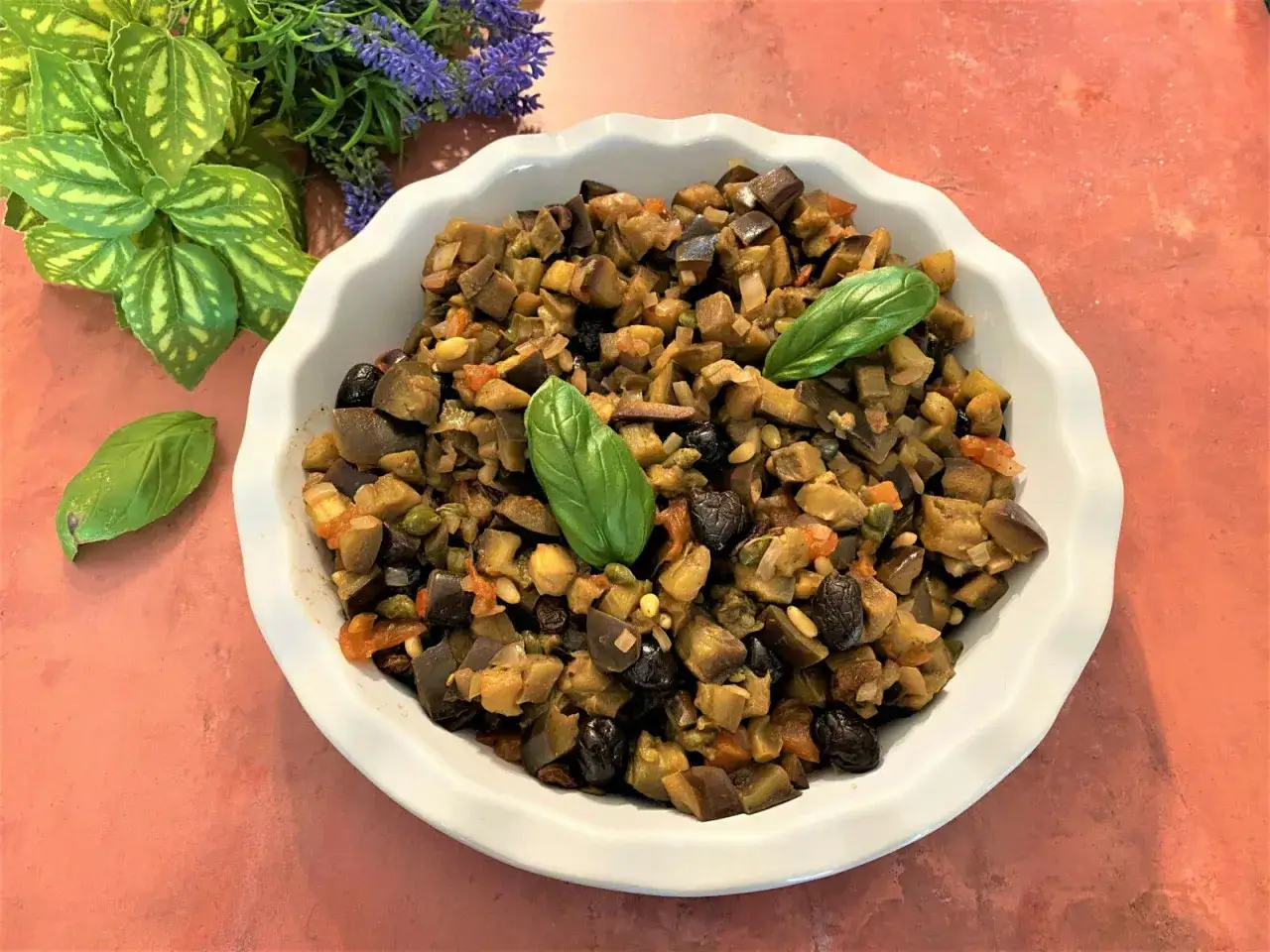 Un plat de caponata sicilienne, m&eacute;lange color&eacute; d'aubergines, olives, tomates et pignons, garni de feuilles de basilic frais.