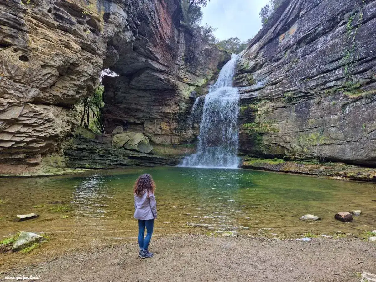 Una mujer admira la cascada y el arco natural de la Foradada en Cantonigr&ograve;s. El agua verde turquesa contrasta con las rocas erosionadas.