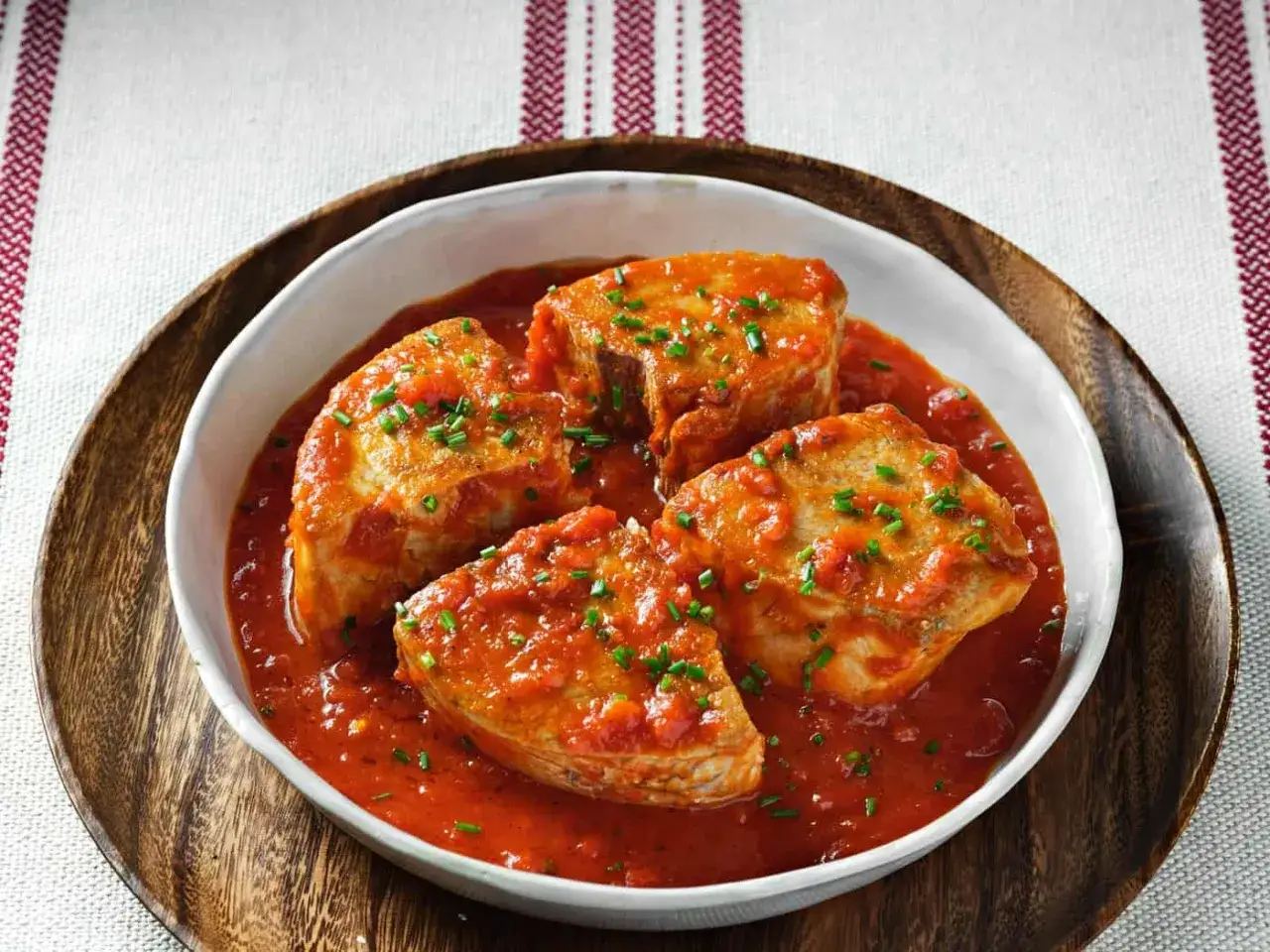 Bonito con tomate, un plato casero y delicioso. Cuatro trozos de pescado en una salsa roja vibrante, espolvoreados con cebollino fresco.