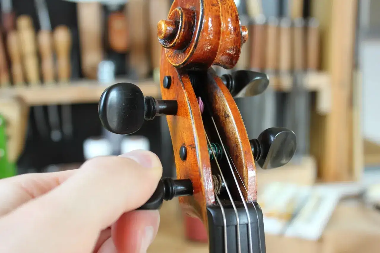 Main d'un musicien ajustant la tension des cordes pour accorder le violon. L'instrument en bois verni est au premier plan.