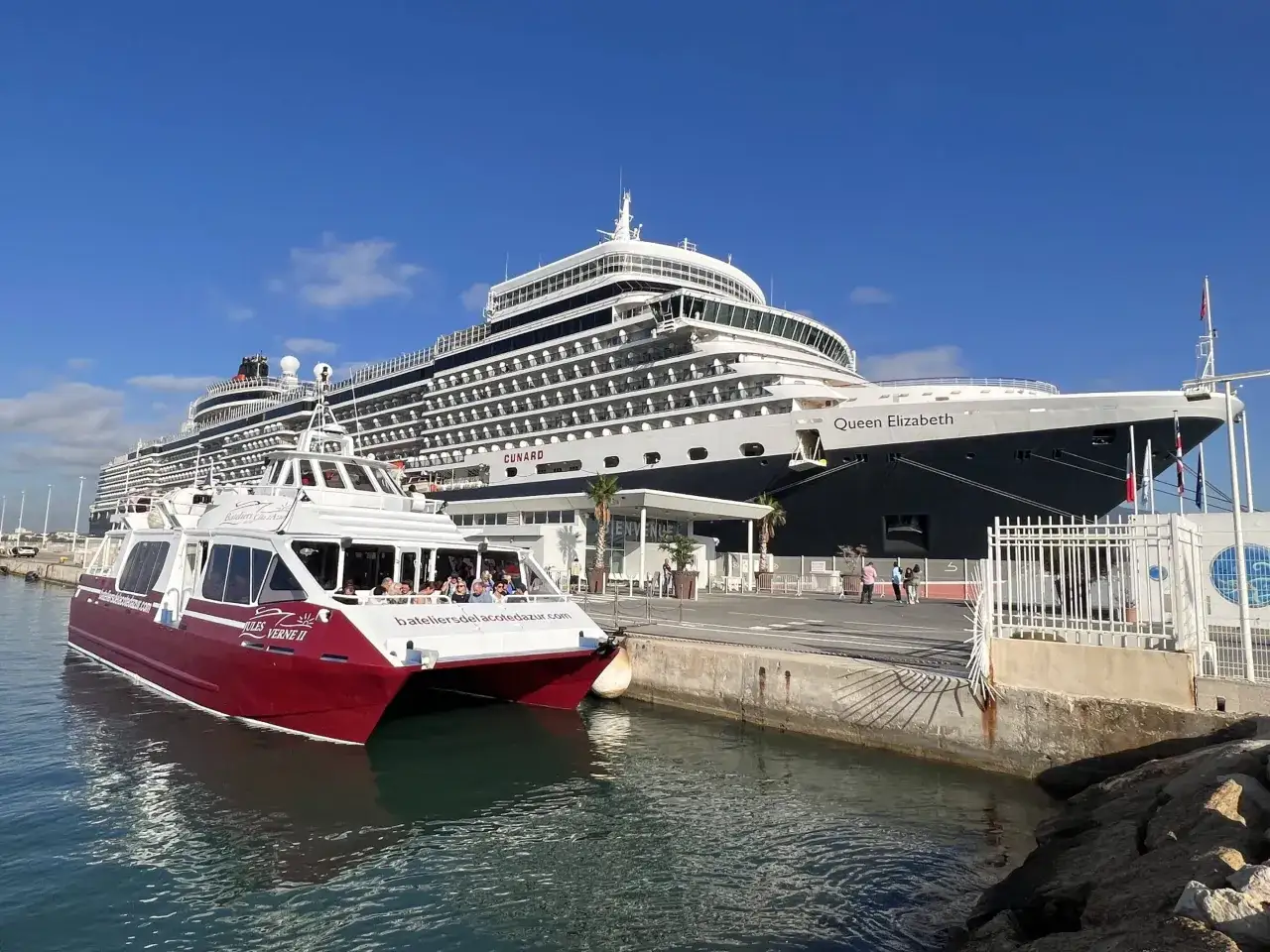La nave Queen Elizabeth attracca nel porto di Tolone, accanto a un battello turistico.
