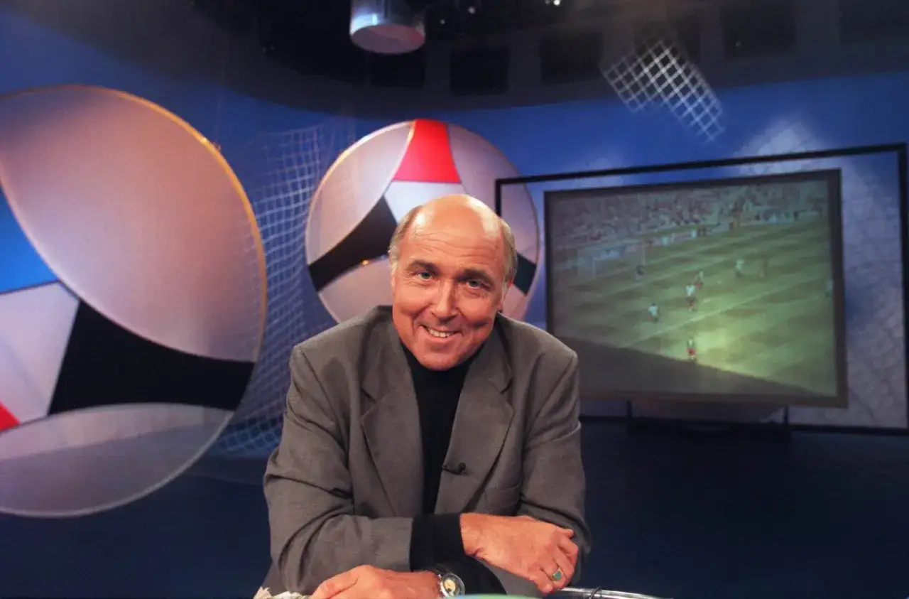 Ingvar Oldsberg ler i studion med fotbollsmål på skärmen bakom.