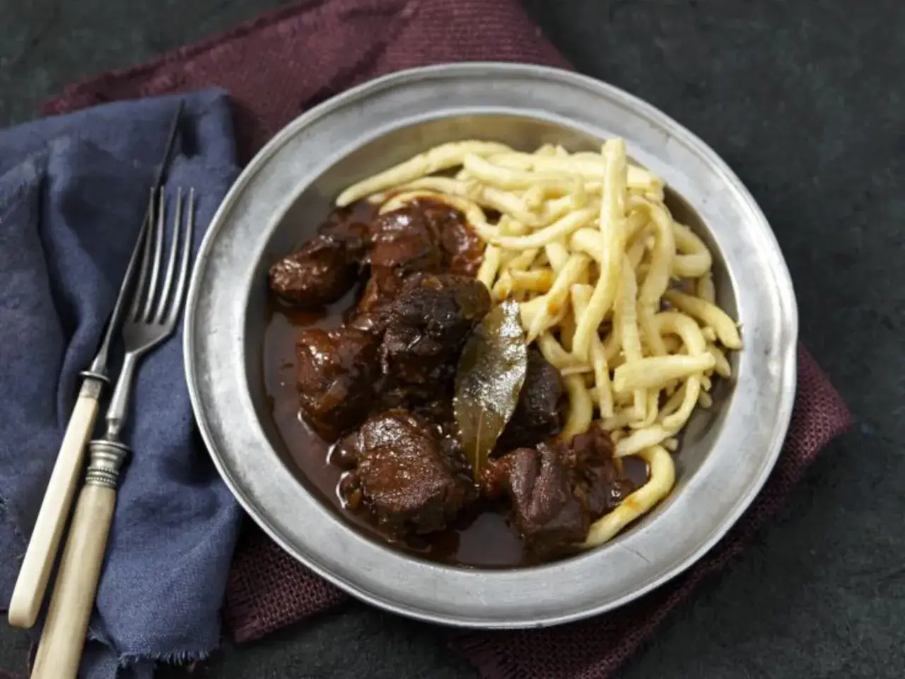 Ein k&ouml;stliches Hirschgulasch-Rezept, wie von einem Sternekoch zubereitet, serviert mit Sp&auml;tzle auf einem Metallteller.