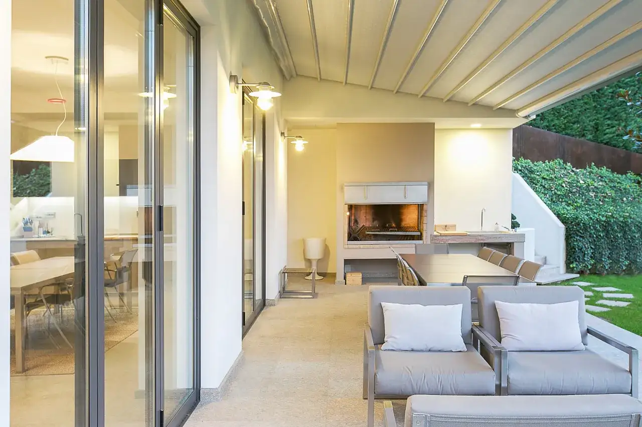 Veranda aperta con camino, tavolo da pranzo e comode poltrone. Idee per arredare una veranda aperta con stile e funzionalit&agrave;.