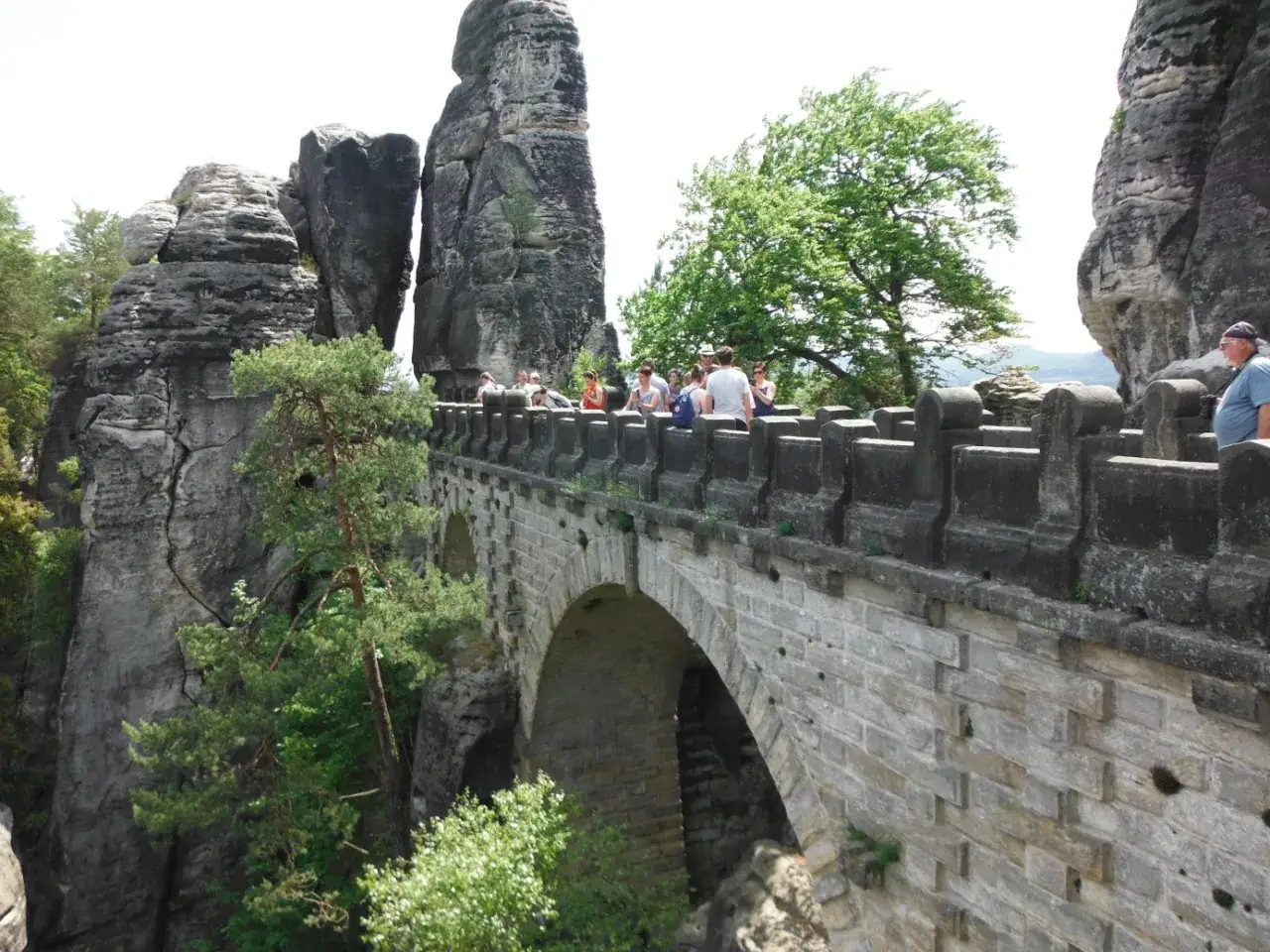 Kamienny most Basteibrücke w Szwajcarii Saksońskiej, z turystami podziwiającymi skalne formacje i zieleń.