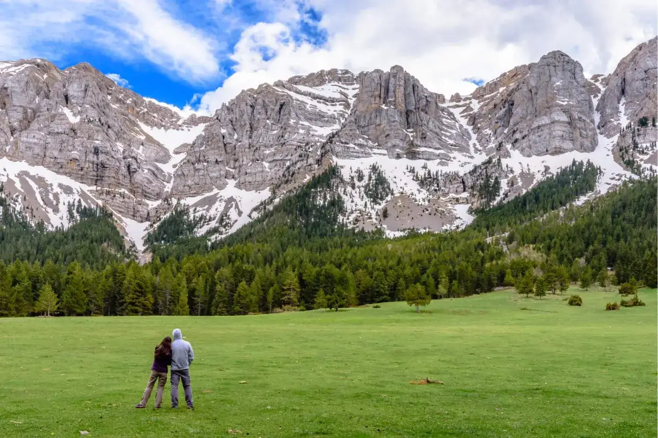 Pareja contemplando el majestuoso paisaje de monta&ntilde;a, con el cadi moixero nevado y un bosque de pinos.