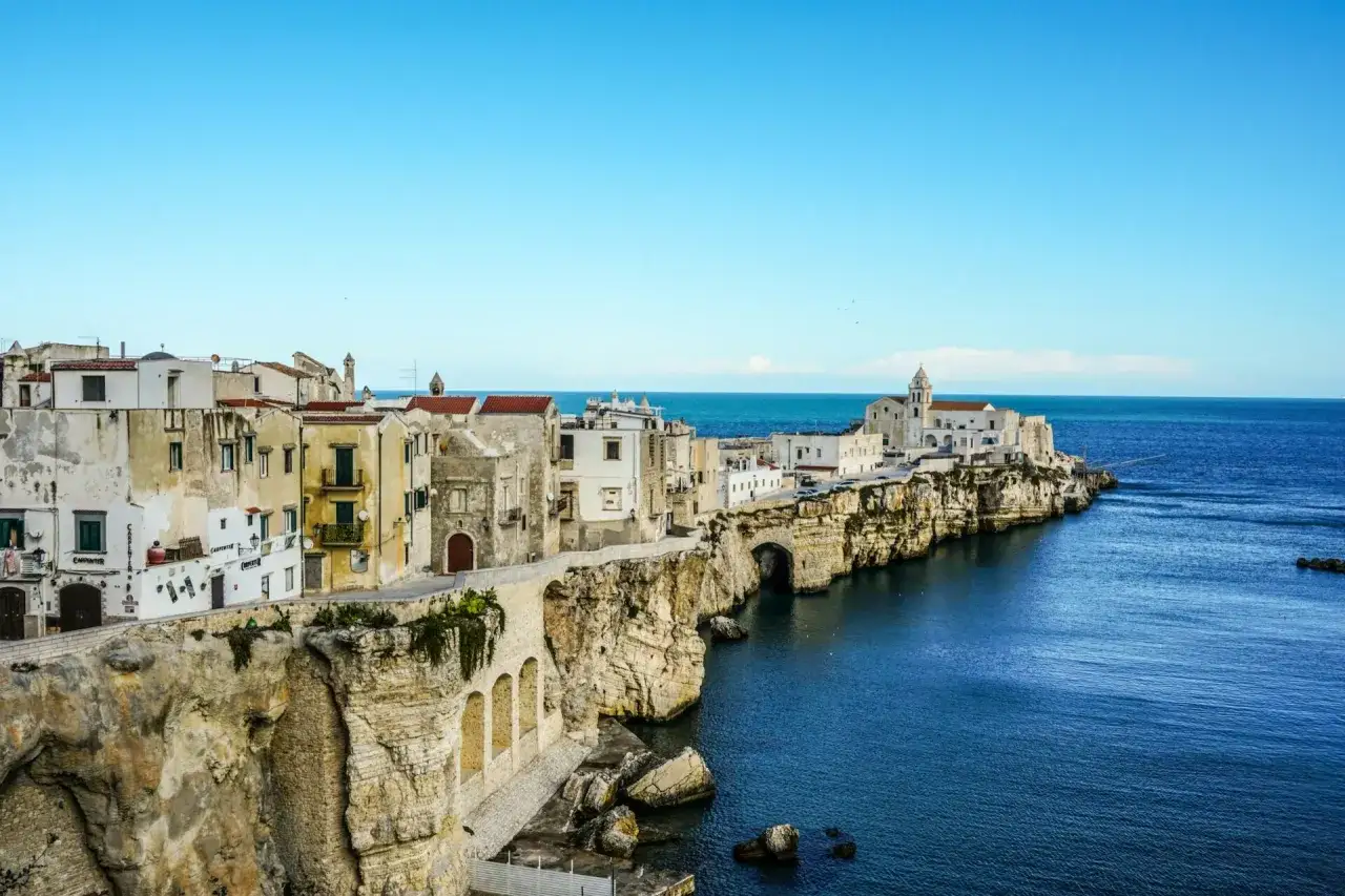 Case bianche aggrappate alle rocce a picco sul mare blu, un borgo pittoresco del Gargano, Puglia.