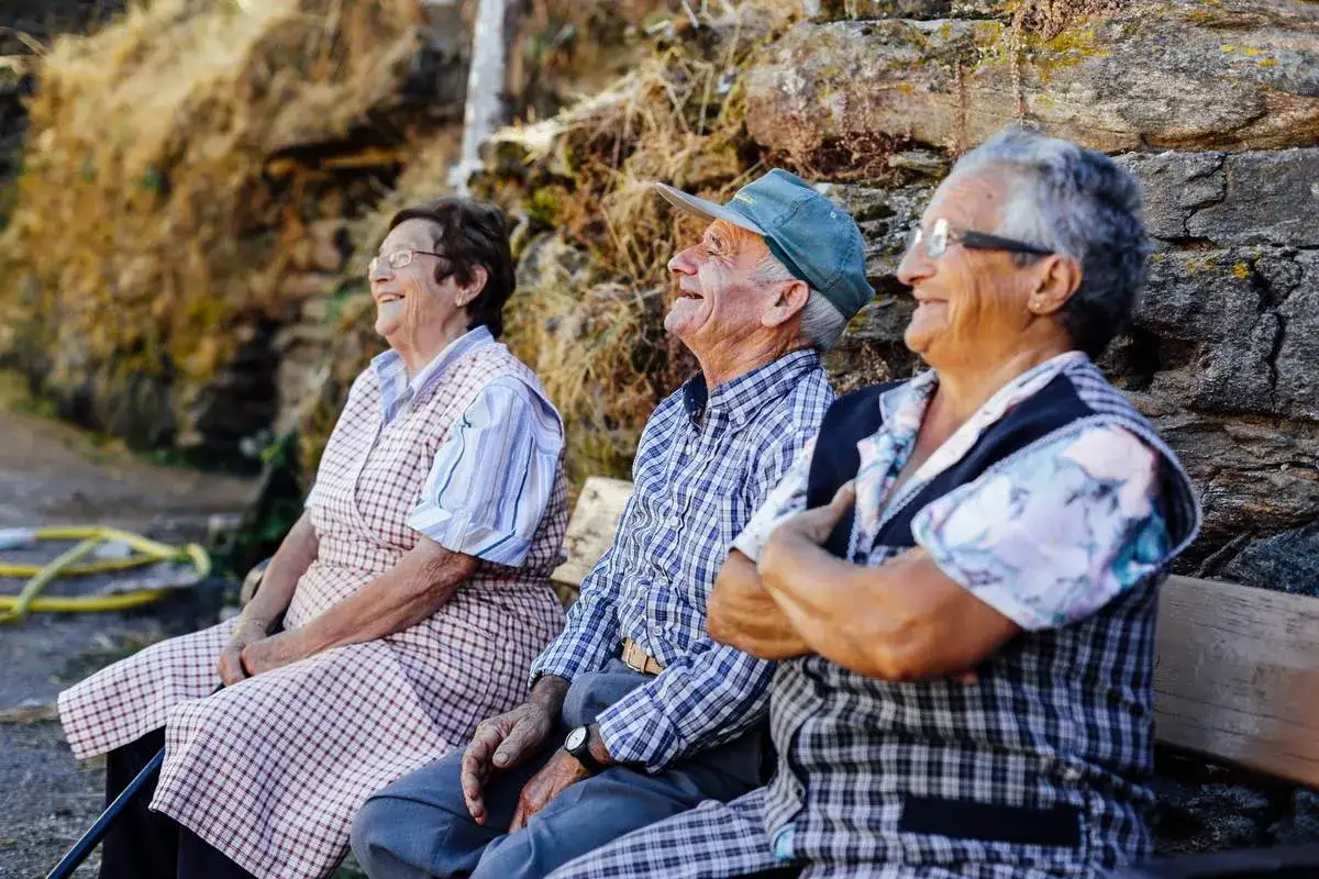 Tres ancianos sonríen sentados en un banco, sus expresiones reflejan la alegría de las expresiones sevillanas.
